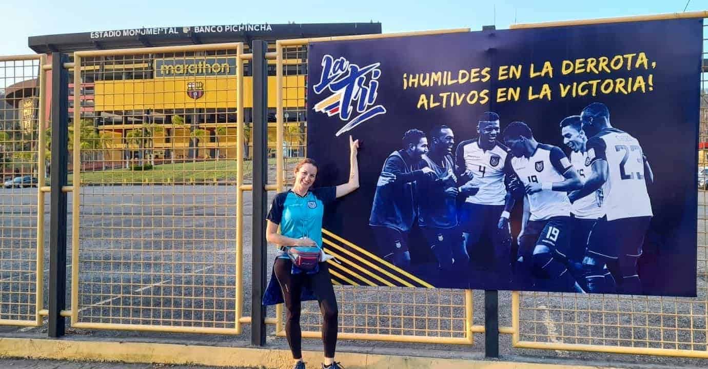 smiling female La Tri fan pointing at poster outside Estadio Monumental