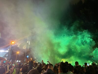 a cloud of green smoke over a crowd of football supporters outside a stadium