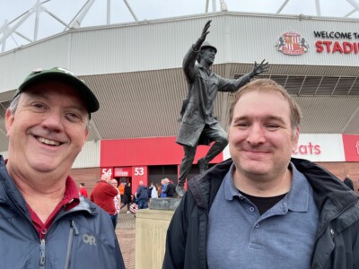 two men in front of a statue outside a football stadium