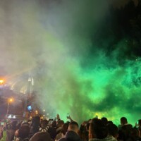 a cloud of green smoke over a crowd of football supporters outside a stadium