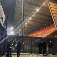 people eating outside a lit-up football ground