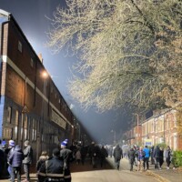 people walking on a street outside an old fashioned football ground