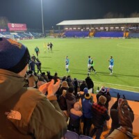 football supporters clapping as players walk off the pitch.